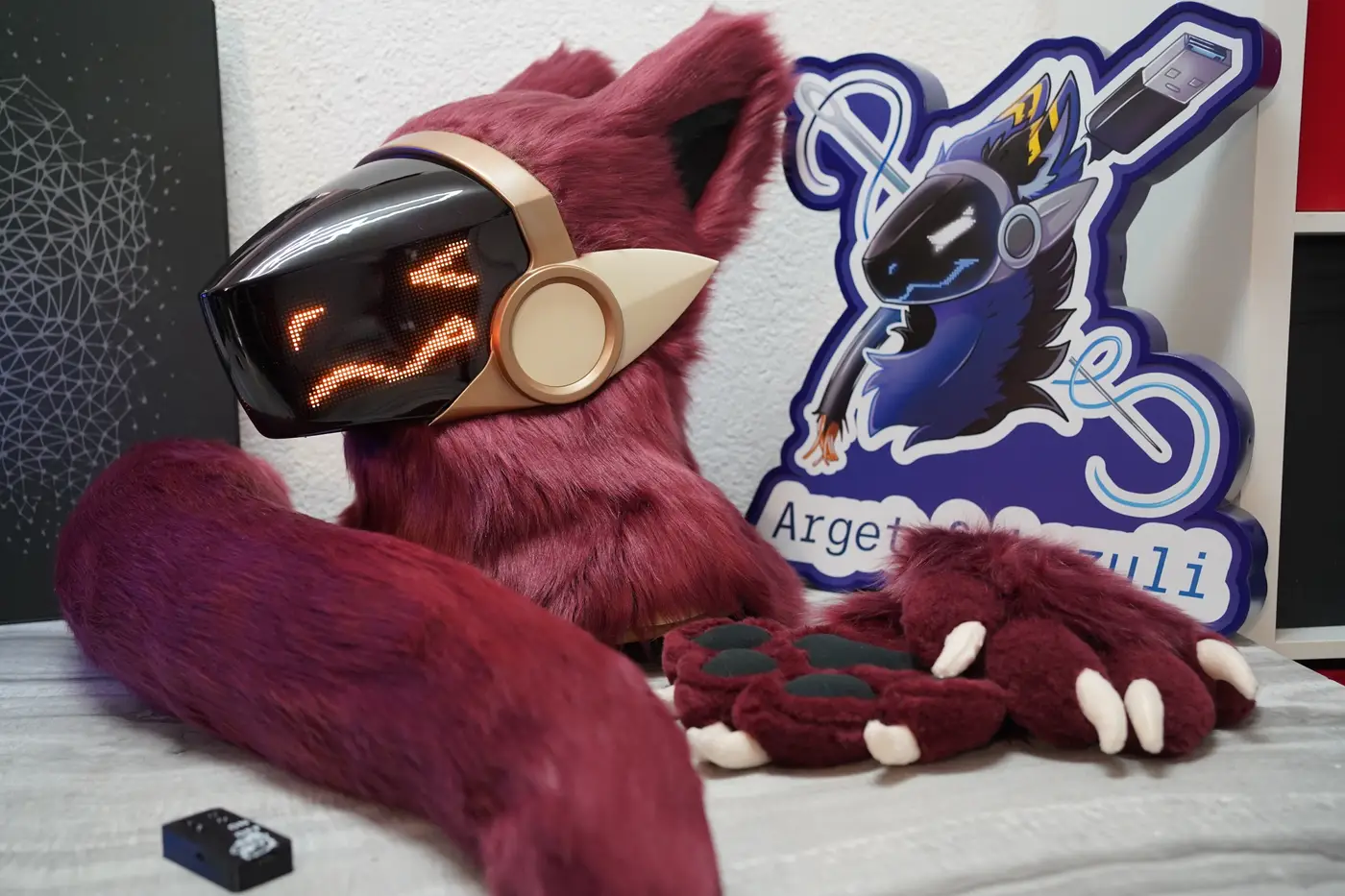 Burgundy Protogen head, hand paws and tail with the Arget and Lazuli logo