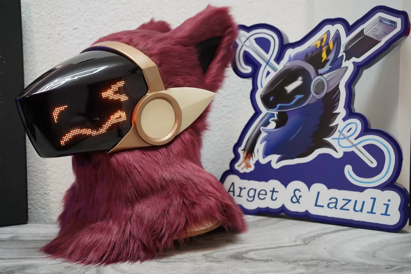 Burgundy Protogen head with an orange face on the cream framed LED visor