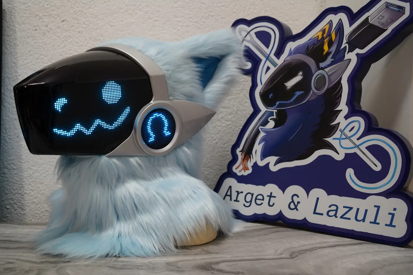 Light blue and silver Protogen head with a round blue pixel eye and a scalloped pixel smile on the LED visor