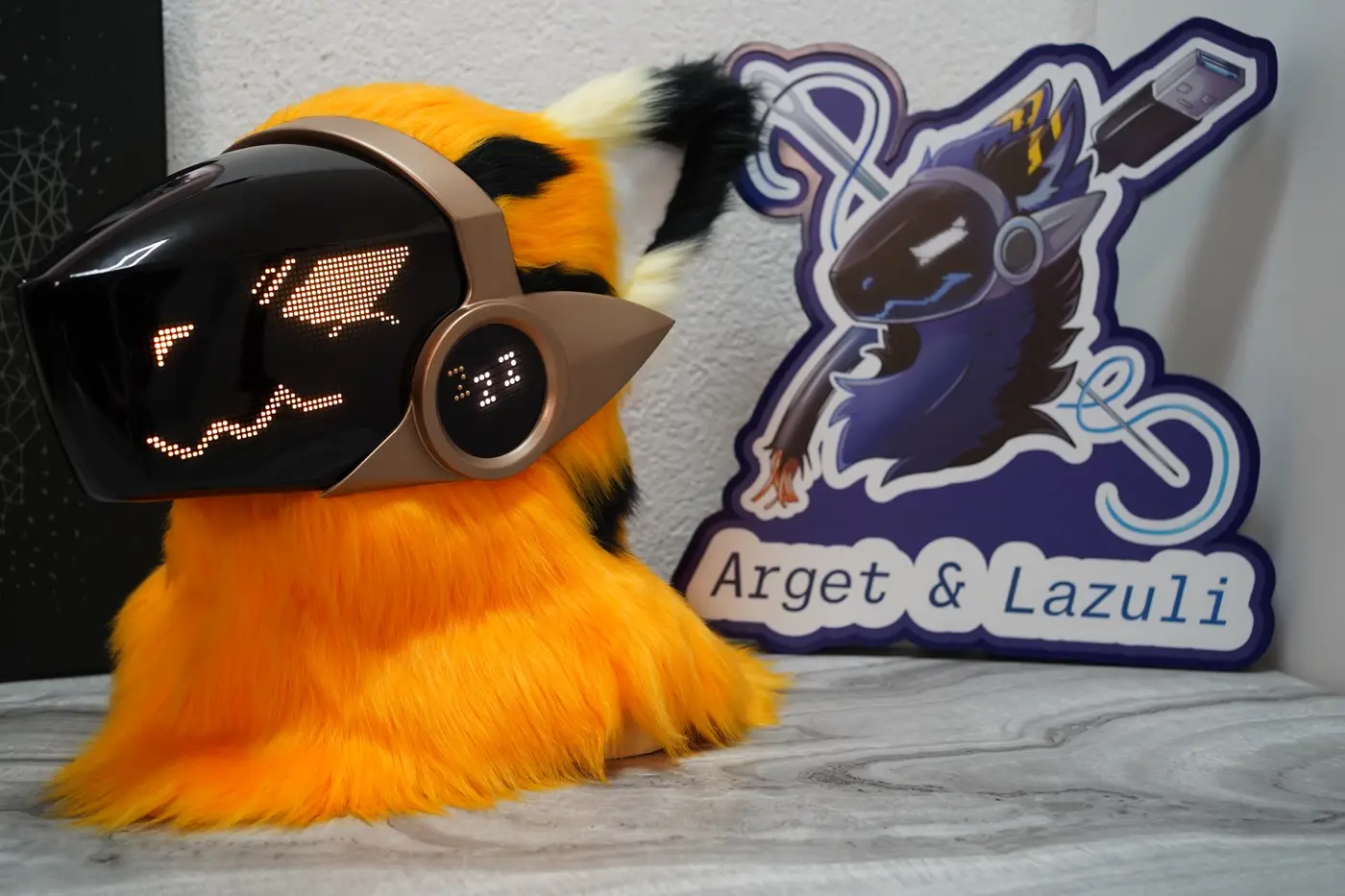 Orange Protogen head with black ear tips and an orange face on the brass framed LED visor