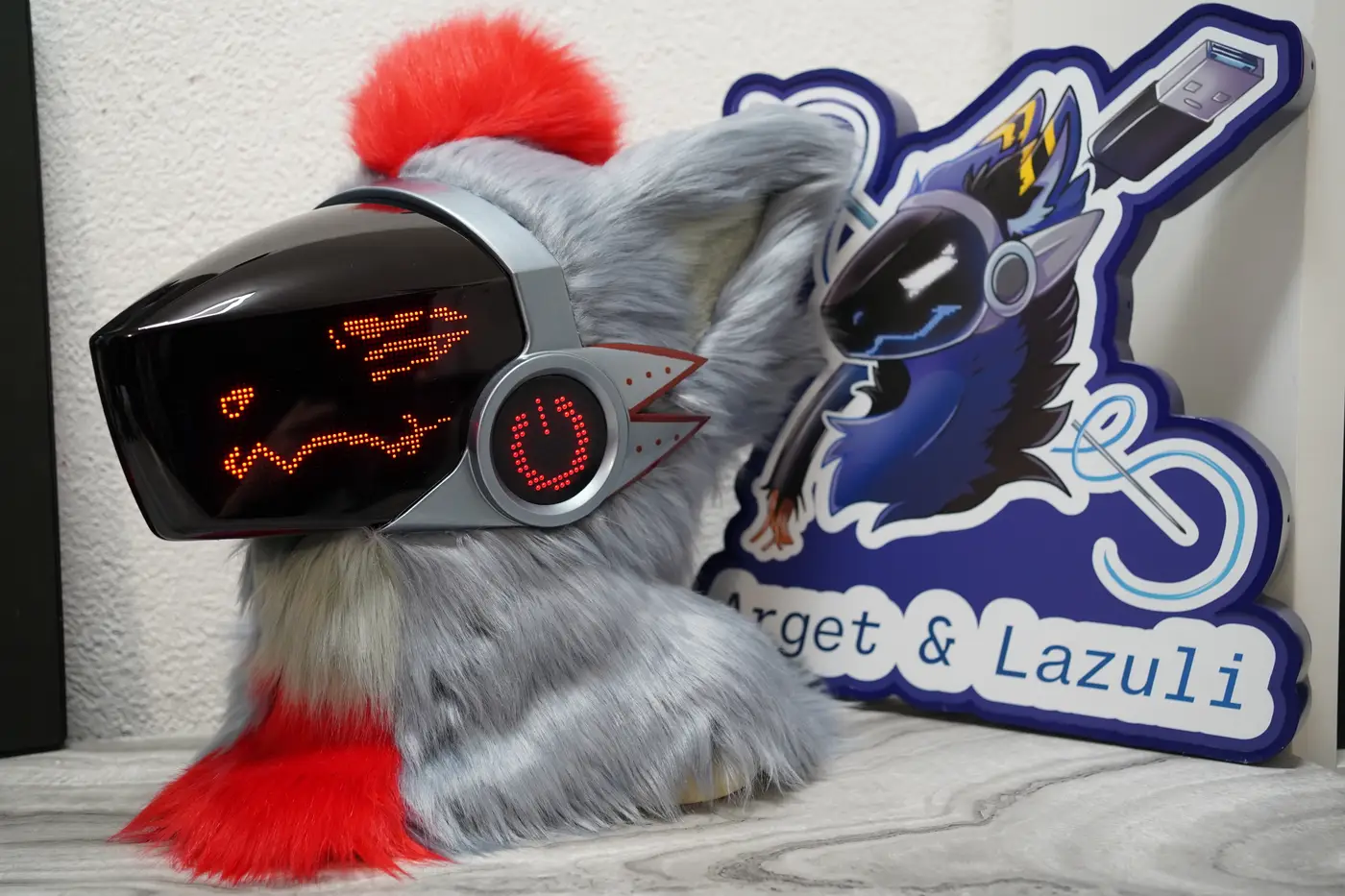 Gray Protogen head with a red mohawk, a narrowed red pixel eye and a wavy mouth on the black LED visor
