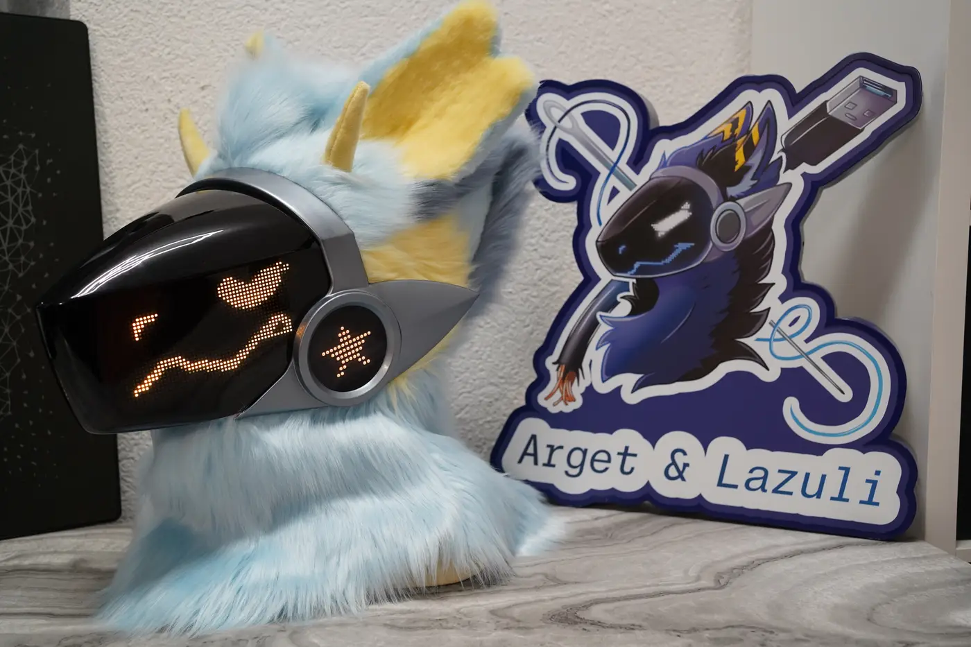 Light blue Protogen head with a curved yellow pixel smile on the black LED visor