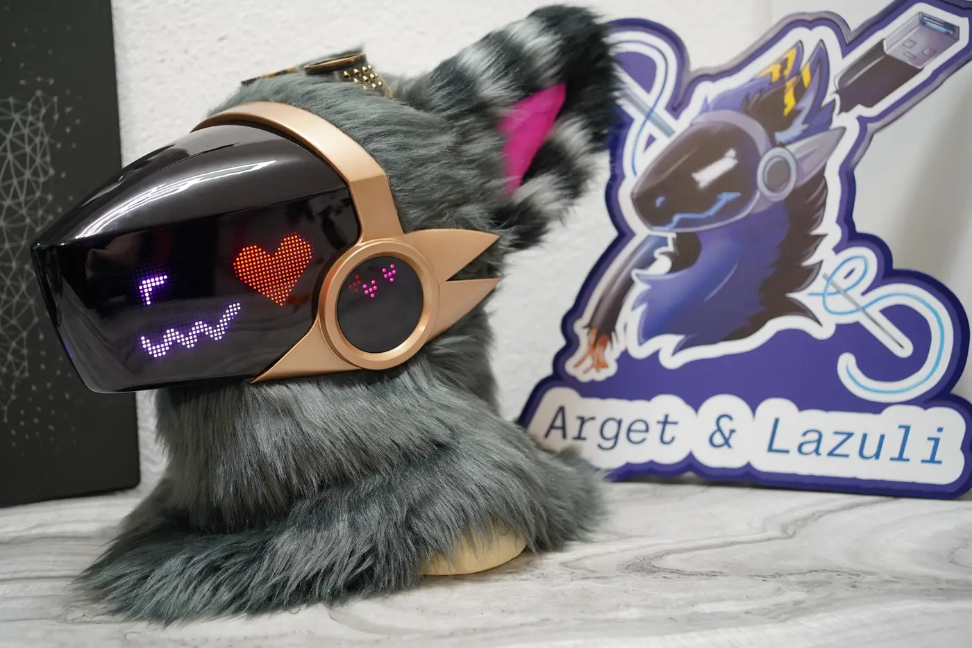 Grey Protogen head with a red heart and a purple wavy mouth on the LED visor