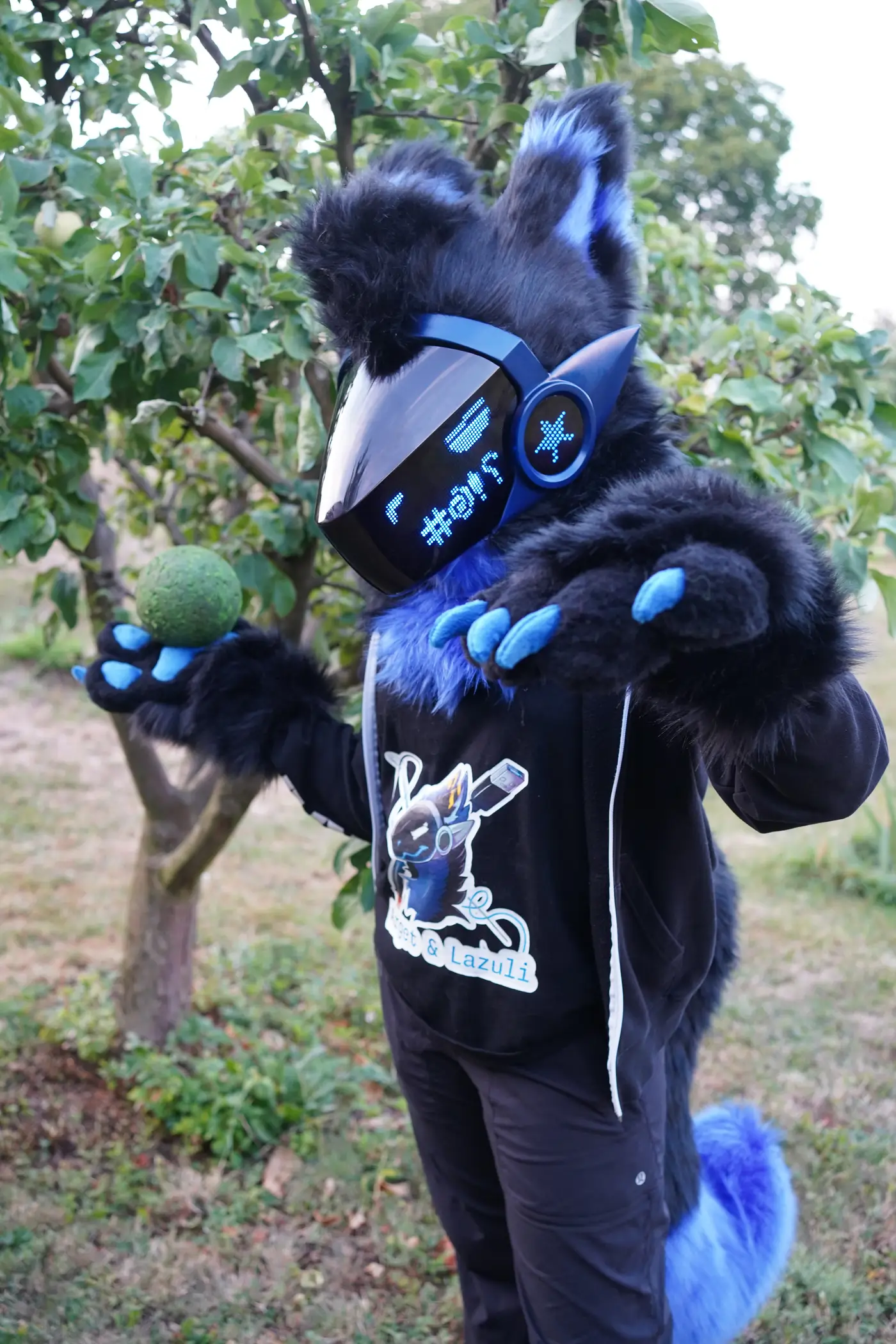 Black and blue Protogen partial in an orchard holding a green fruit, pixel symbols on the blue LED visor