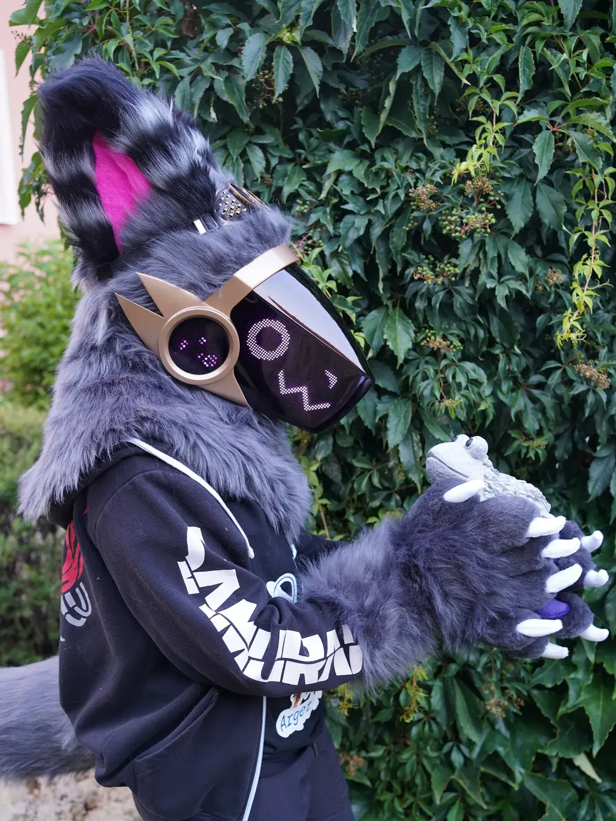 Grey Protogen full partial by an ivy wall holding a small white figure, purple face on the brass framed LED visor
