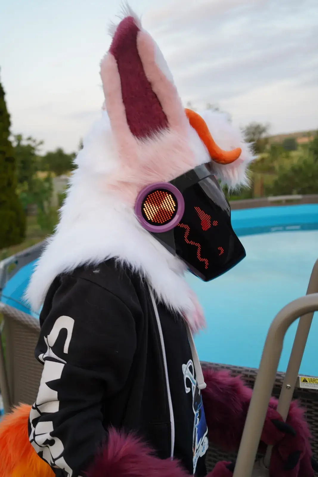White and pink Protogen mini partial by a garden swimming pool, side view with a red face on the LED visor