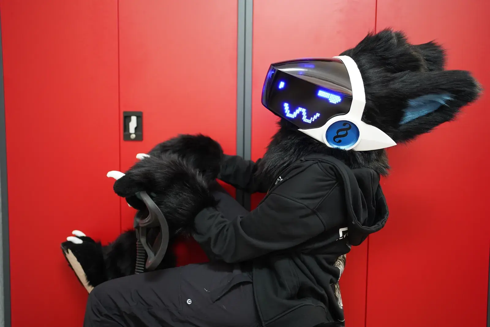 Black Protogen partial with white visor showing a blue wavy pixel eye pattern and a blue ear badge