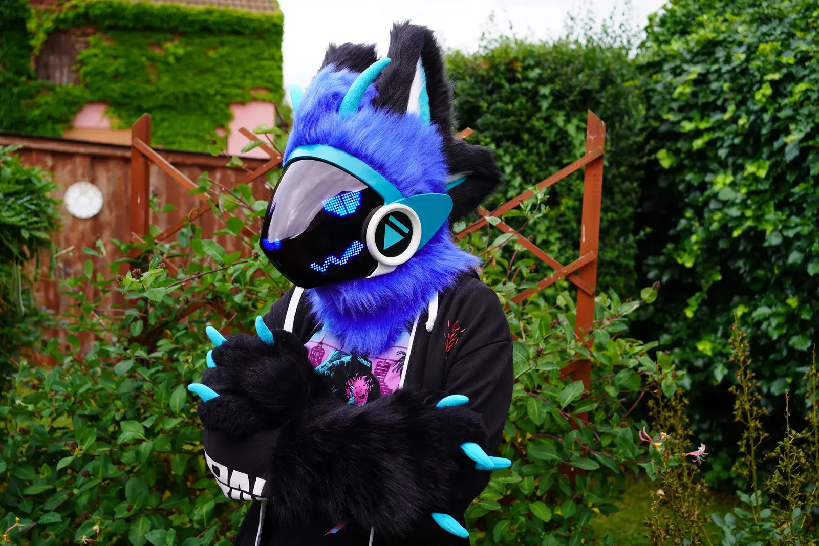Blue and black Protogen partial with teal ear tips and blue wavy pixel eyes in a garden setting