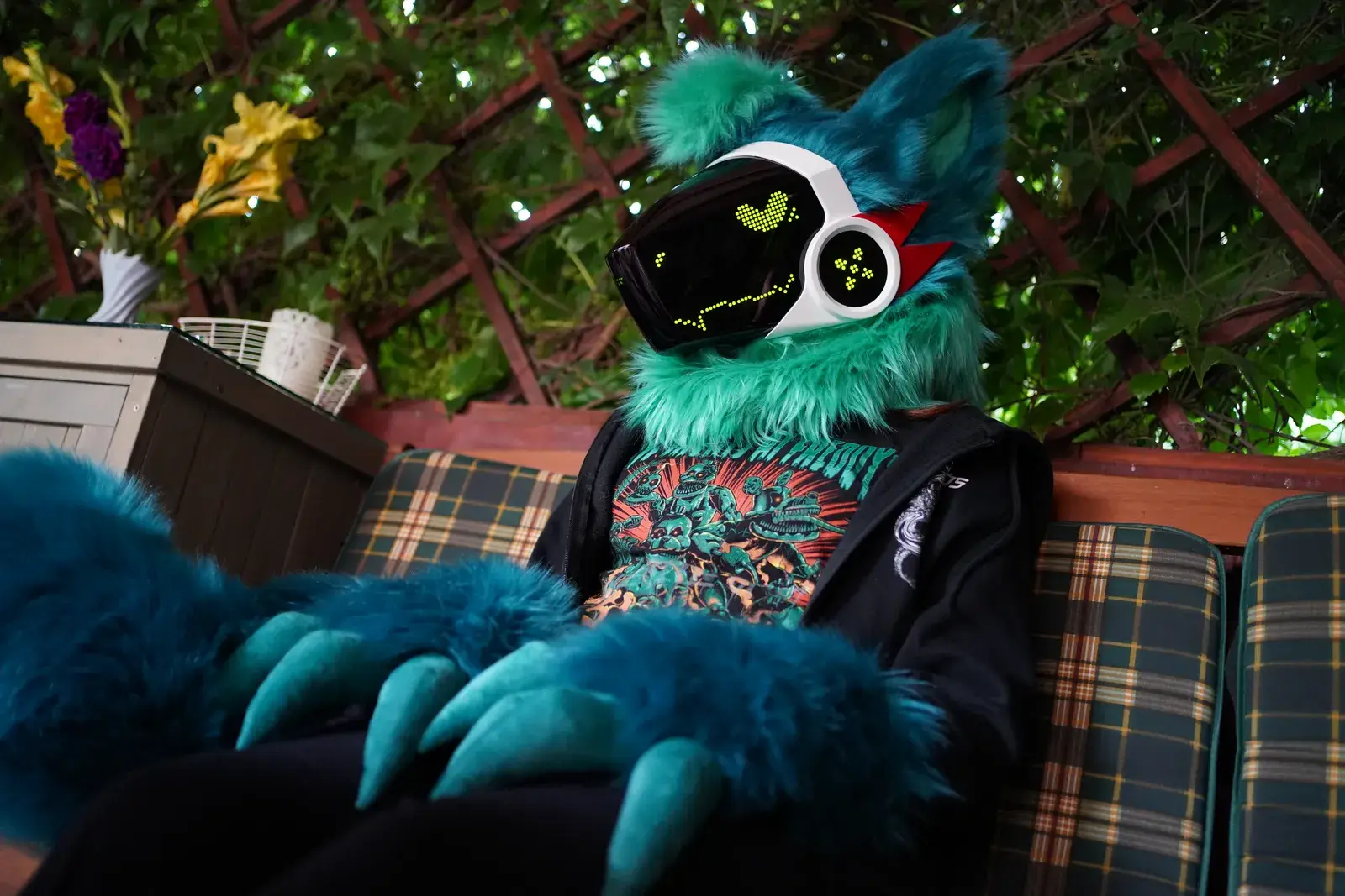 Teal Protogen partial reclined on an outdoor bench, white visor showing yellow green pixel eyes