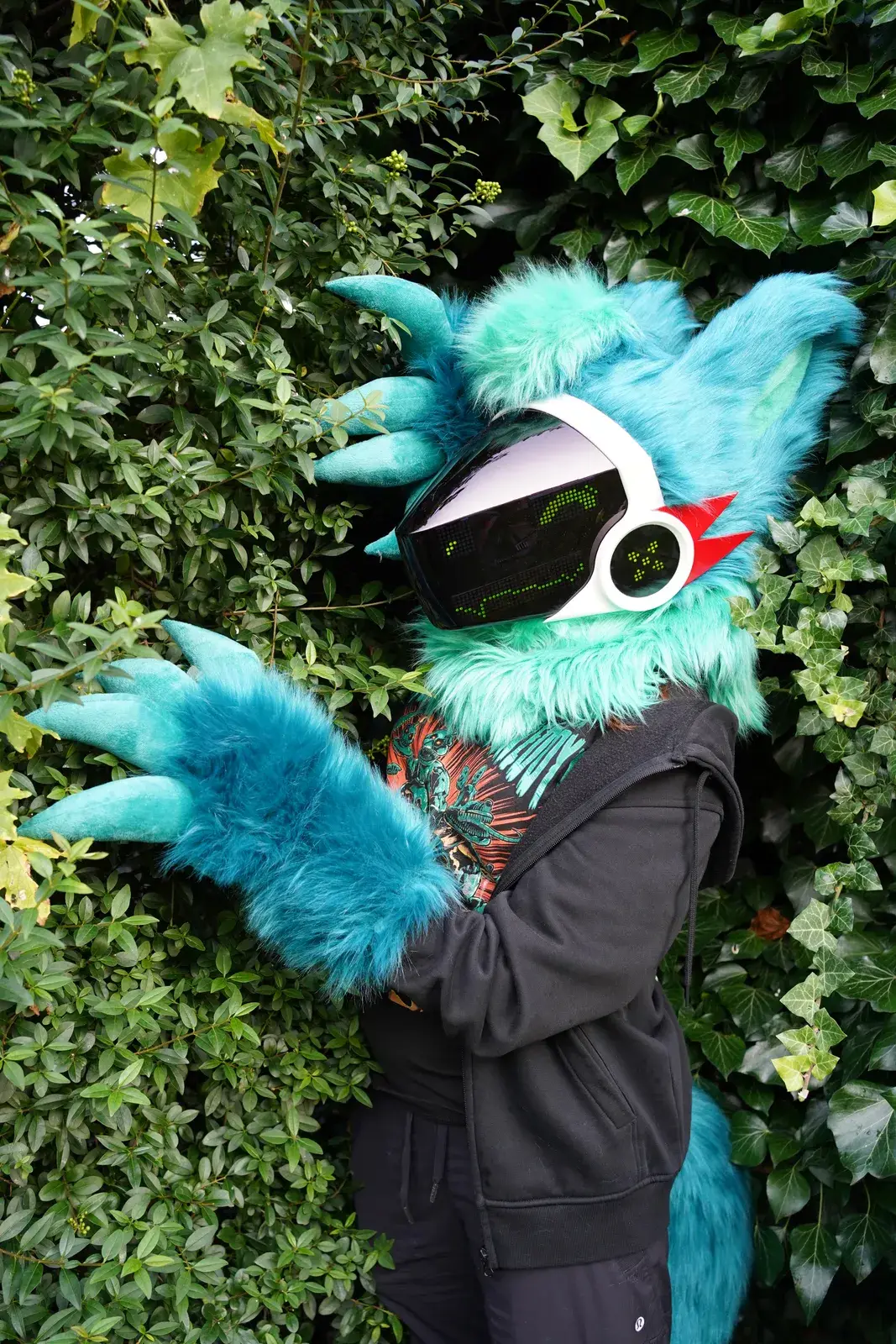 Teal Protogen partial raising large clawed paws in front of an ivy hedge, green pixel visor