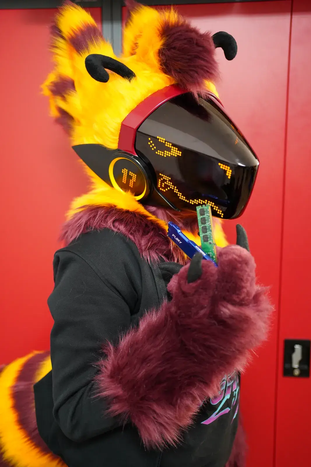 Yellow and dark red Protogen partial in side profile holding a RAM stick, black visor with an amber LED face and black antennae