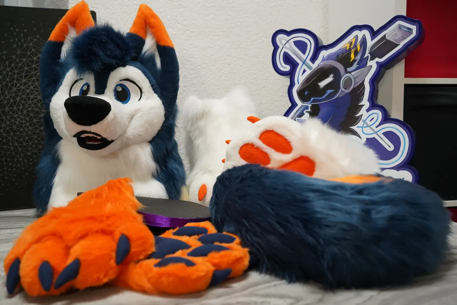 Navy blue, white and orange toony husky head with blue eyes and orange ear tips, laid out indoors with matching handpaws and a branded standee