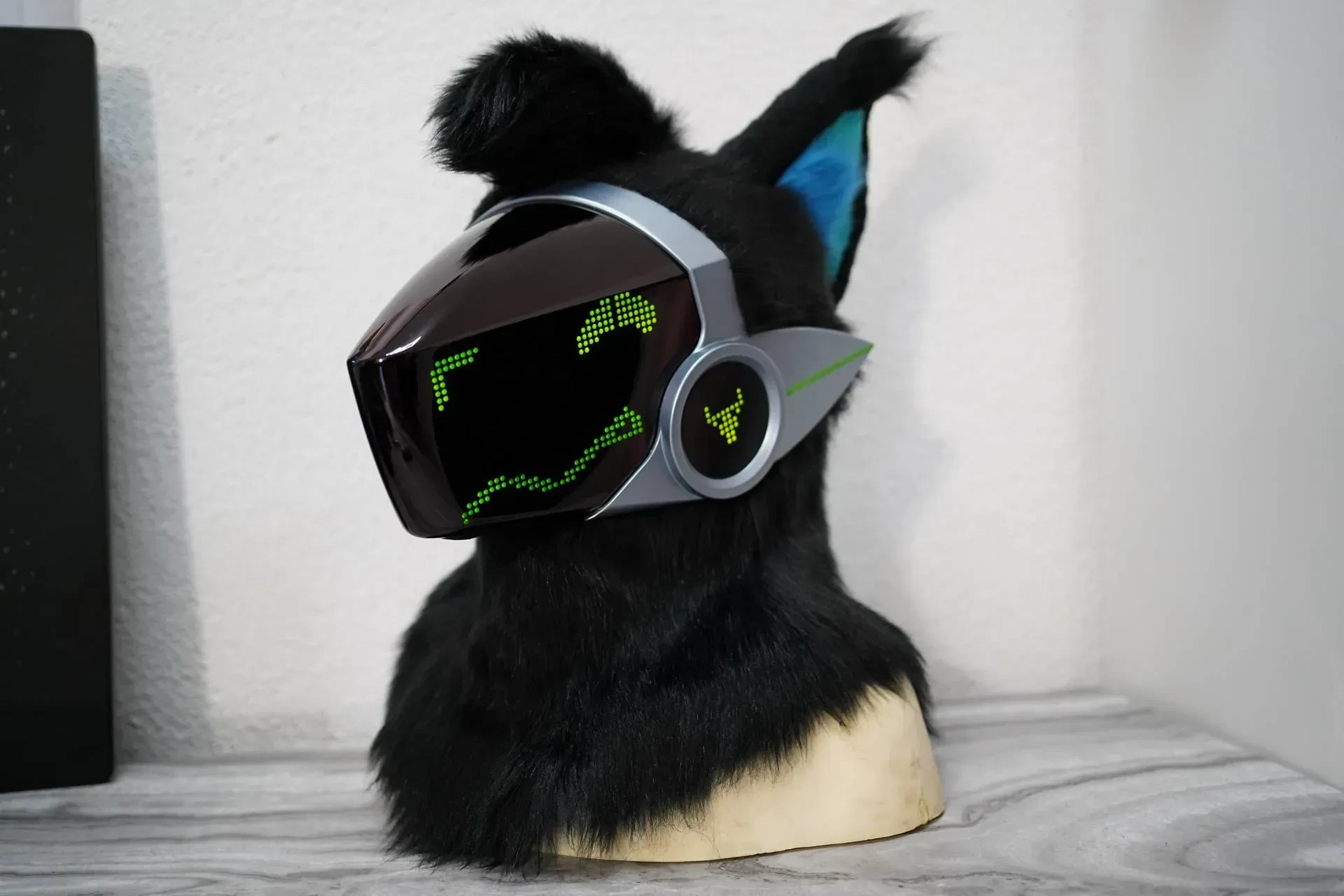 Black Protogen head on a stand, silver visor with green pixel eyes and teal ears, by Arget & Lazuli