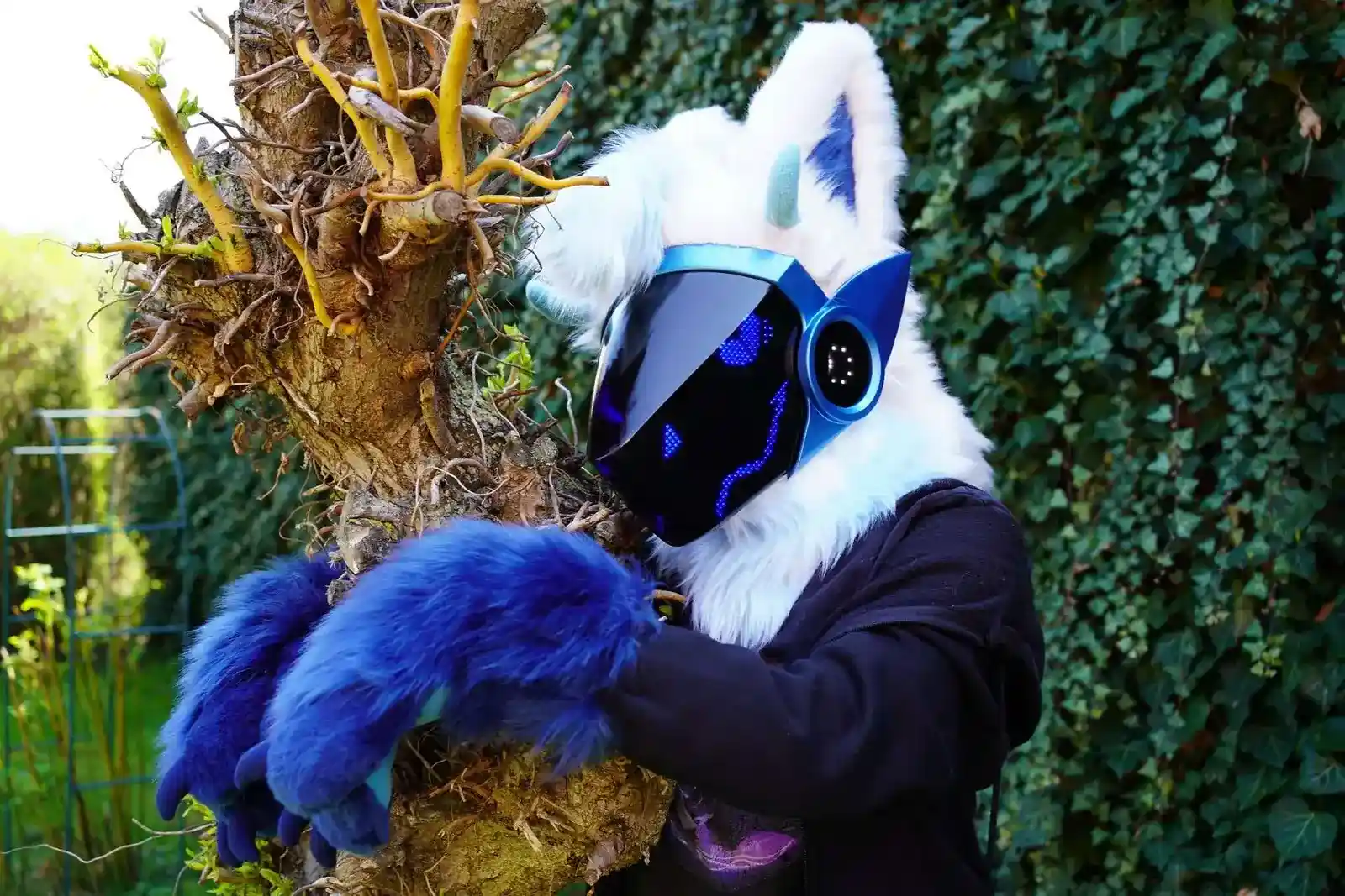 White and blue custom Protogen fursuit head with a blue LED visor and blue clawed paws, handmade by Arget & Lazuli